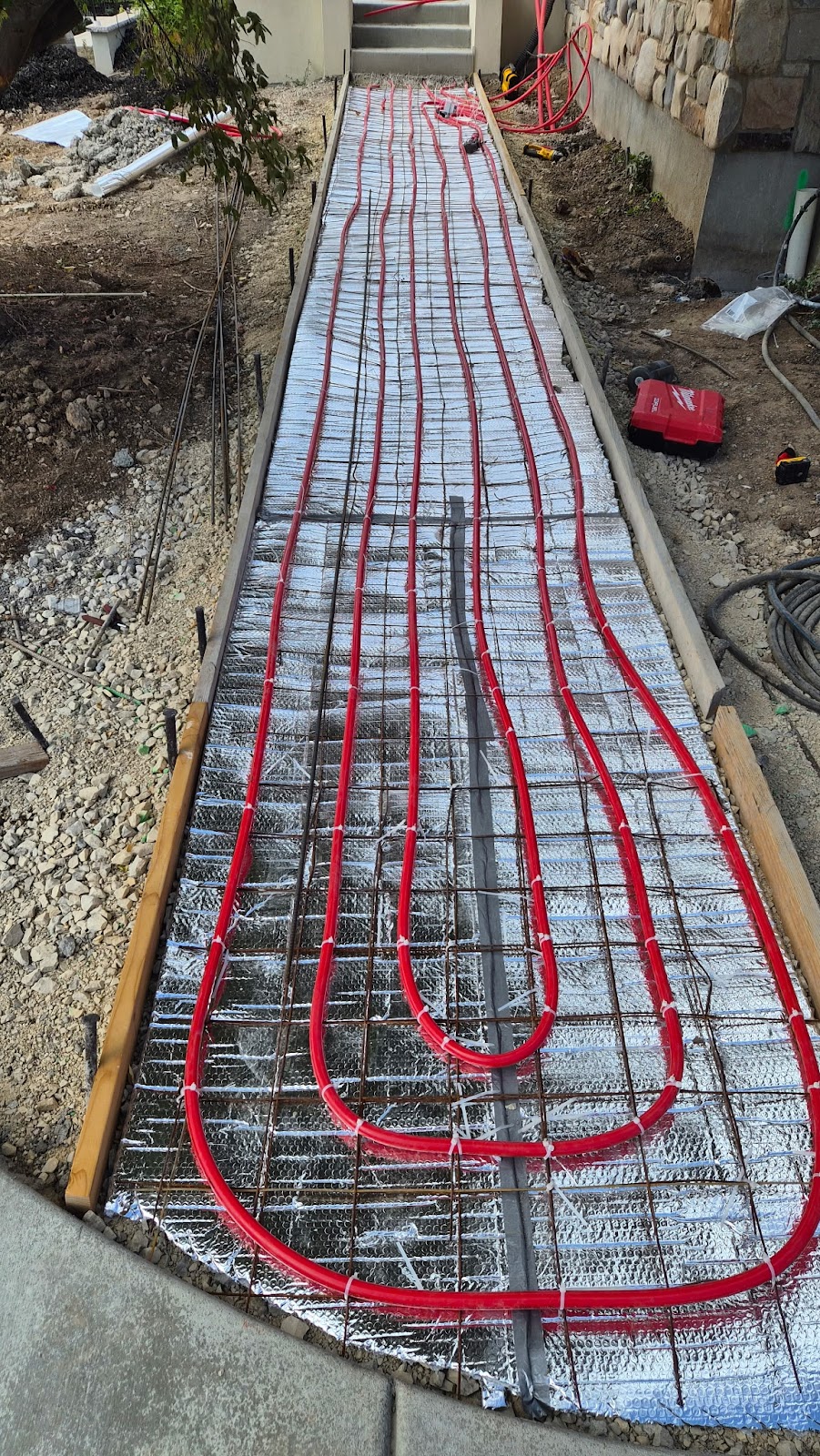 Red radiant heating tubes are installed in a grid pattern on a walkway in Park City, utilizing advanced hydronics technology and covered with reflective insulation by Glacier Plumbing before the concrete is poured.