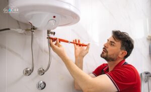 A man uses a wrench to adjust pipes connected to a wall-mounted water heater in a tiled bathroom, demonstrating the skills of true plumbing and heating experts in Salt Lake City.