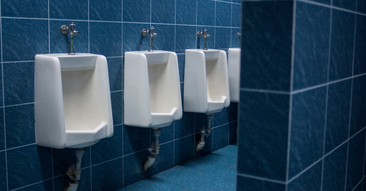 Four white urinals are mounted on a blue tiled wall in a public restroom, with a partial view of a dividing privacy wall - illustrating the attention to detail you’d expect from top Plumbing professionals and Heating Experts in Salt Lake City.