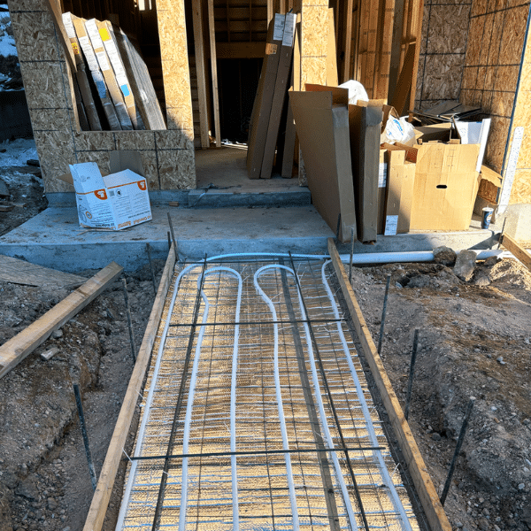 A construction site shows radiant heating pipes installed in a rebar grid, ready for concrete pouring at the entrance—perfect for heated driveways. Discover if heated driveway cost is justified and are heated driveways worth it for your project.