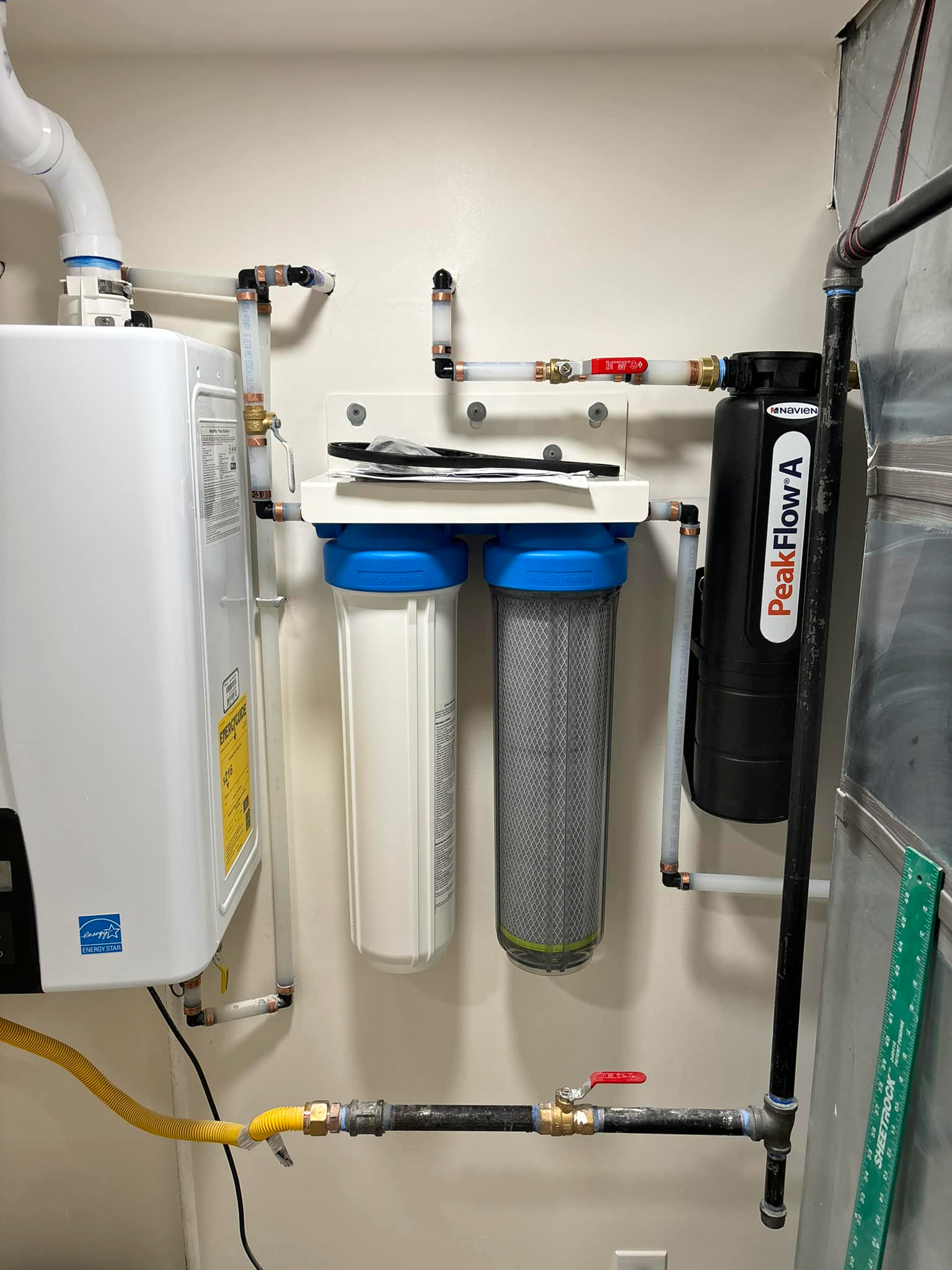 Water filtration system with two large filter cartridges, a black PeakFlow cylinder, and connected pipes mounted on a white wall in a utility room, expertly installed by Plumbing and Heating Experts in Salt Lake City.