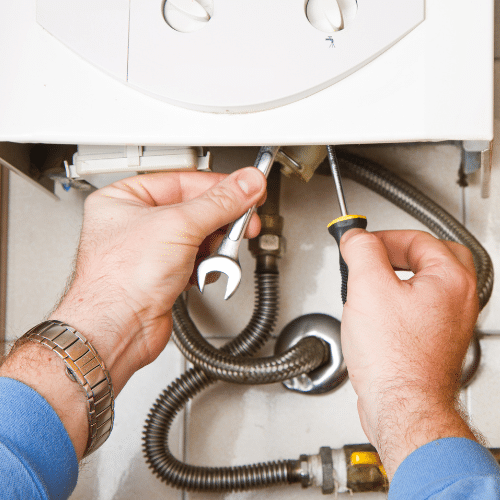 Hands using a wrench and screwdriver to repair or adjust parts of a tankless water heater or gas boiler in Utah, with visible pipes and fittings.