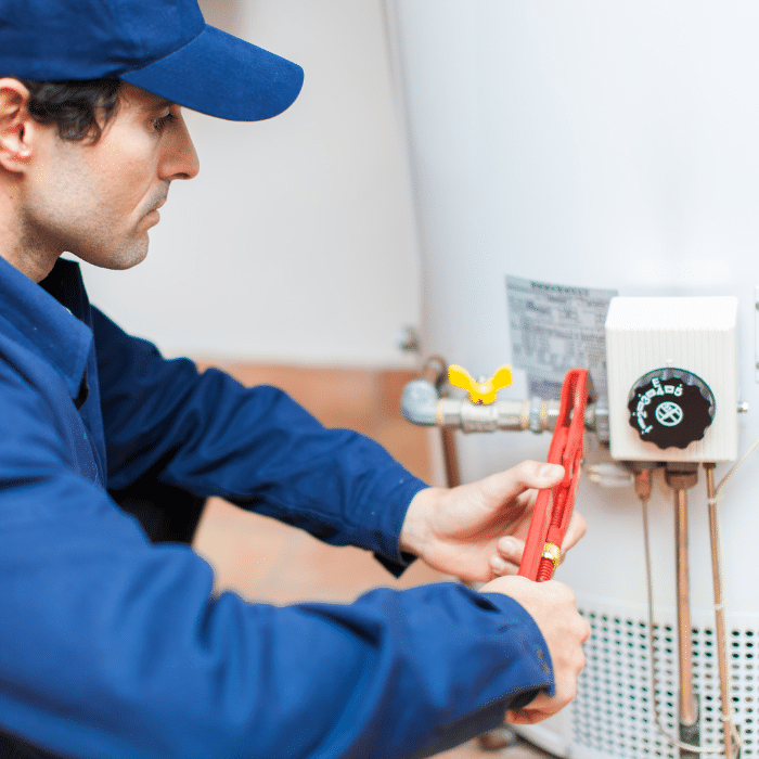 A technician in blue uniform uses a pipe wrench to perform water heater repair, adjusting plumbing on a water heater.