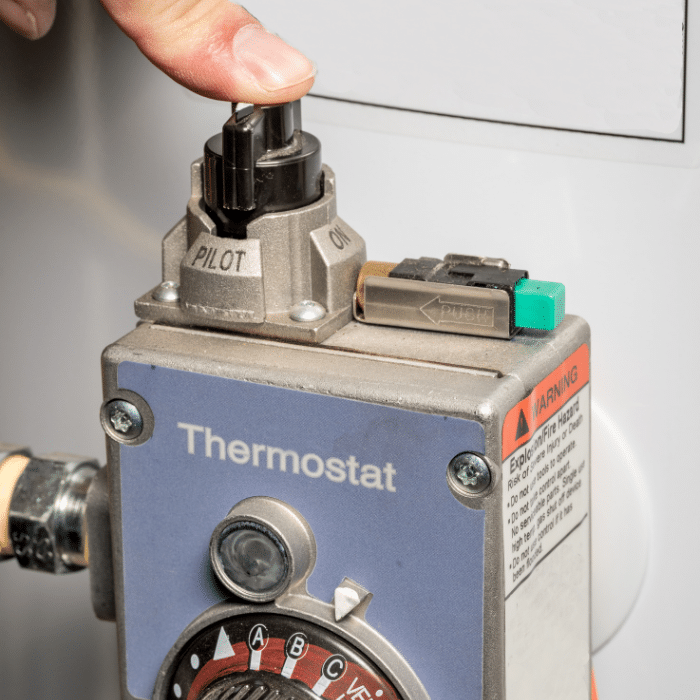 A hand turns the control knob on a thermostat labeled with "PILOT" and "ON" settings during a water heater repair.