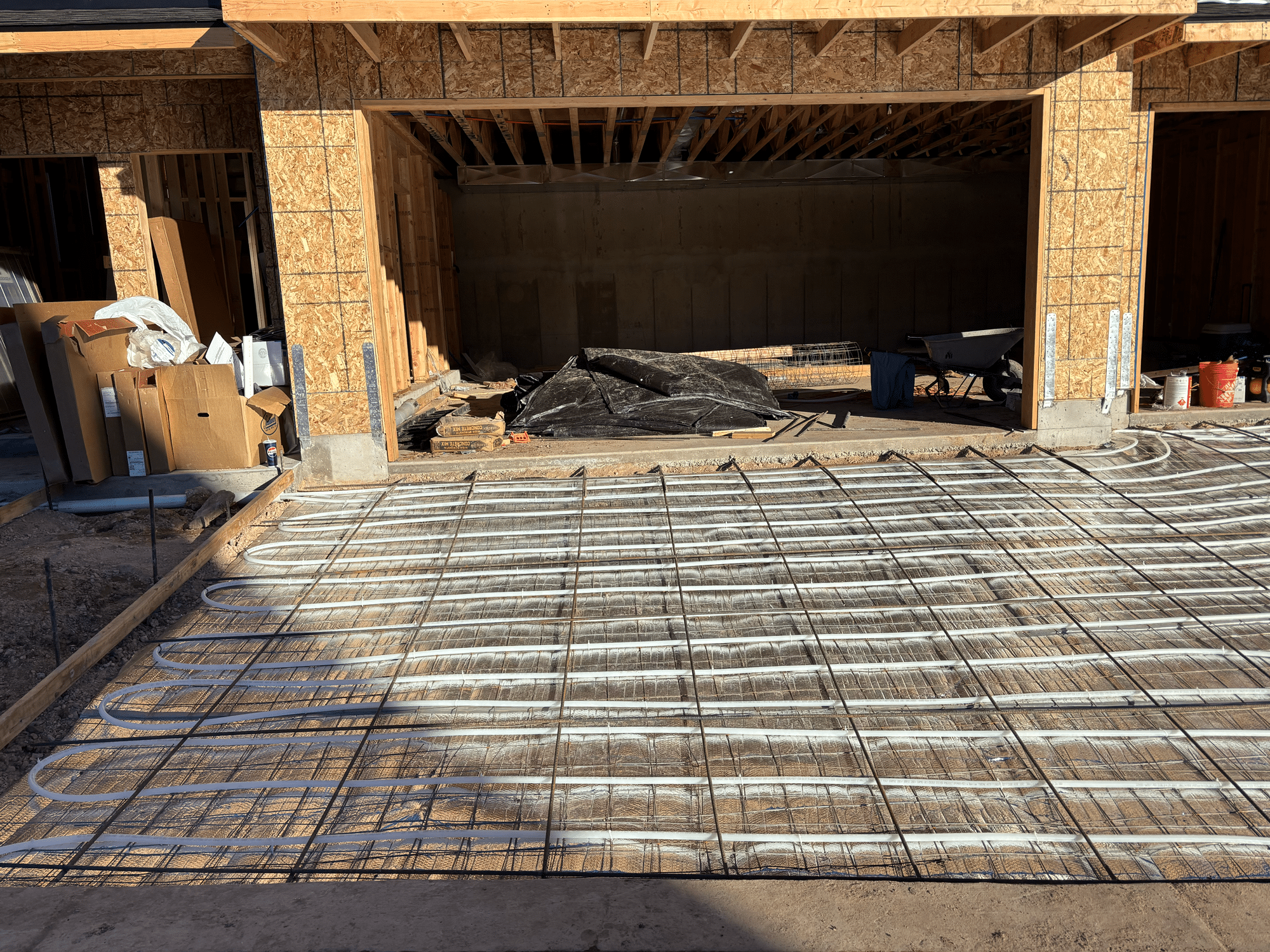 Heated driveway installation showing exposed radiant tubing and rebar grid in front of an unfinished garage under construction, expertly handled by heating experts in Salt Lake City.