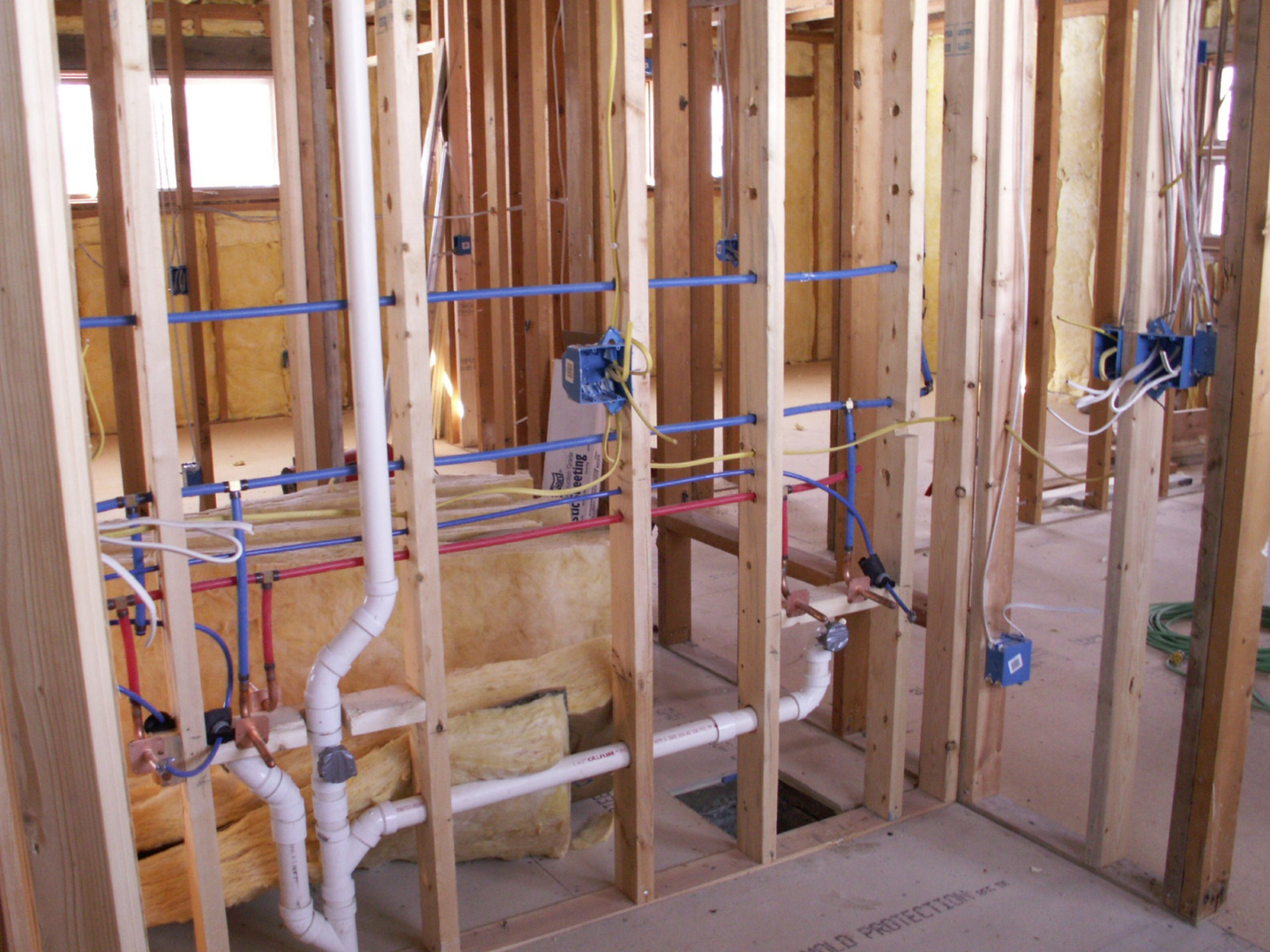 Exposed wood framing, electrical wiring, and plumbing pipes in the interior of a house under construction - an essential stage often inspected by Plumbing and Heating Experts in Salt Lake City.
