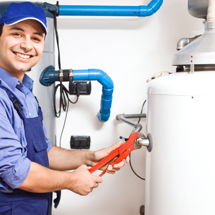 A plumber in blue uniform uses a red wrench for water heater repair; blue pipes and valves are visible in the background.